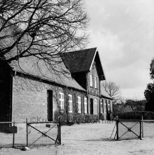 Volksschule: vorn Schulhof mit Zaun: rechts oben Baumäste