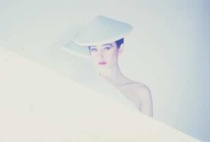 Model in Schaumstoffmode : Model mit hellblauem Schaumstoffhut hinter einem Neonleuchtkörper