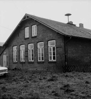 Sühlen: Volksschule: rechts Sirene auf Dach: davor verkrautete Wiese: links Pkw