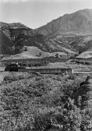 Landschaftsblick : Etwa 25 km östlich an der Küste Bejaias. An den Berghängen befinden sich Macchiebüsche. Im Vordergrund ist eine mit Geröll bedeckte Brücke zu erkennen.