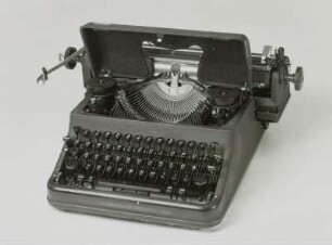 Typenhebelschreibmaschine "Rheinmetall". Vorderanschlag (sofort sichtbare Schrift), Universaltastatur, Farbband. Schrägansicht von vorn, Deckel über Typenhebelsatz aufgeklappt