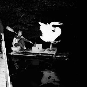 Karpfenfest: Neuhöfer Teich: Nachtaufnahme: Wasserrevue "Der verhexte Karpfenteich": Schwan auf Floß mit Paddeler: im Wasser Spiegelung: links Geländer von Steg: hinten Bäume, 10. Oktober 1965