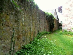 Kirchhof im Westen mit Kirchhofmauer (Wehrgang mit Steinbrüstung und hölzernem Laufgang abgetragen) im Verlauf nach Norden mit Werksteinen im Mauersteinverband