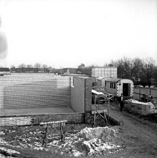 Dörfergemeinschaftsschule: Erweiterungsbau: links Rohbau mit Grundmauern: davor Holzböcke und Gerüst: rechts Bauwagen, Lkw und Baumaterial vor Bauzaun: hinten Schulgebäude, Bäume und Wohnhäuser