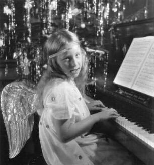 Kinderbilder. Als Engel kostümiertes Mädchen am Klavier vor dem Weihnachtsbaum