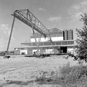 Hartsteinwerk: vor Fertigstellung: in der Mitte und links Brücke mit Laufkatze: dahinter Werkhalle: vor der Halle Stapel mit Steinen: rechts hinten im Eingang Mann