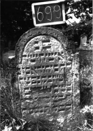 Grabstein 699 (Index: 100104850) Material: Sandstein Zustand: stark verwittert, abgeblättert, teilweiser Textverlust Maße HxBxT: 94x59x8 cm Beschreibung: Stele, eingezogener Rundbogenabschluss, Schriftfeld eingetieft: Grabstein 699