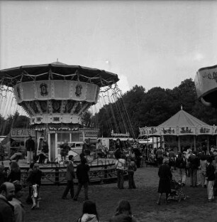 Frühjahrsmarkt: Volksfest: Exer: vorn links Jugendliche auf Kettenkarussell: davor und dahinter Besucher vor Jahrmarktsbuden: hinten Bäume