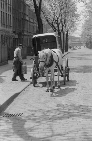 Eine Pferdekutsche am Straßenrand und ein Mann mit einer Milchkanne