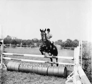 Sportveranstaltung: 2. Pferdeleistungsschau: Veranstalter Reitverein Ahrensburg/Hamburg-Ost: Reiter zu Pferd bei Sprung über Hindernis: Blechtonnen: im Hintergrund Zaun