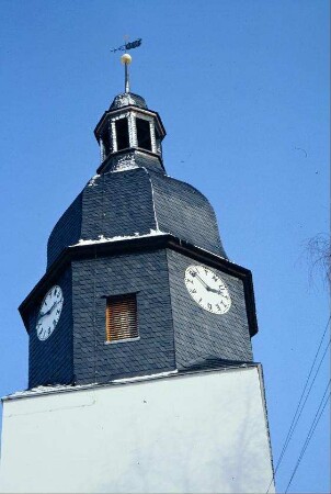 Kirchturmspitze mit Uhr; Zifferblatt zeigt anstelle Zahlen Buchstaben: NUTZEDIEZEIT