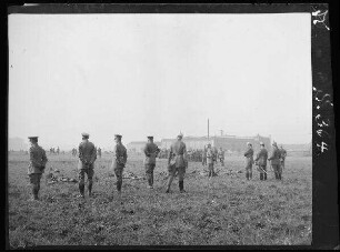 Bousbecque (Dep. Nord, Frankreich): Soldaten auf einem Feld beim Liegendschießen, dahinter und daneben beobachtende Offiziere, im Hintergrund ein Fabrikgebäude ("Brigadekommandeur General von Klaus besichtigt Offiziersaspirantenkurs")