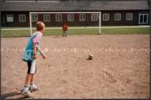 Auf einem Fußballsandplatz, Junge schießt auf ein Tor mit Torwart (Prämiertes Foto G)