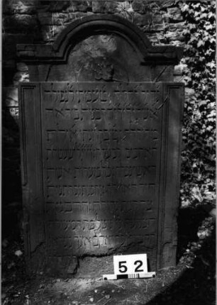 Grabstein 52 (Index: 99629553) Material: Sandstein Zustand: unten abgeblättert/Textverlust Maße HxBxT: 115x70x11 cm Beschreibung: Stele mit eingeschnürtem eingezogenem Segmentbogenabschluß mit Verdachung Symbolik: vierblättrige Blüte: Grabstein 52