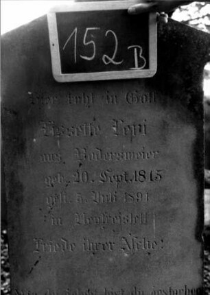 Grabstein 152 (Index: 100111310) Material: Sandstein Zustand: leicht verwittert Maße HxBxT: 170x60x30 cm Beschreibung: Stele, getreppter Sockel, giebelartiger Abschluß mit Verdachung, rechteckiges Schriftfeld eingetieft Symbolik: Kranz mit Schleife: Grabstein 152B