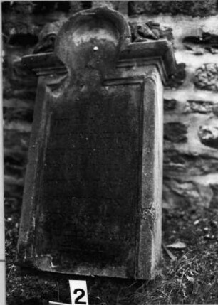 Grabstein 2 (Index: 99804491) Material: Sandstein Zustand: vom Sockel gebrochen, stark verwittert Maße HxBxT: 96x59x25 cm Beschreibung: Stele, eingezogener Segmentbogenabschluß mit Verdachung, Eckakrotere: Grabstein 2
