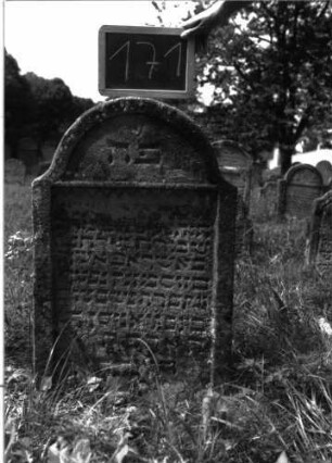 Grabstein 171 (Index: 100103390) Material: Sandstein Zustand: stark verwittert Maße HxBxT: 80x54x8 cm Beschreibung: Stele, Konvexbogenabschluss, Schriftfeld rechteckig eingetieft, oben durch Zackenfries begrenzt, im Bogenfeld eingeritzte Blüte Symbolik: Blüte, Zackenfries: Grabstein 171