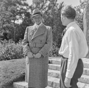 Mann in Hut und Mantel im Park vor einem Denkmal
