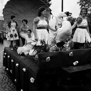 Karpfenfest: Umzug: Festwagen, Neptunia auf Muschelthron, Nymphen, Schwan: dahinter am Straßenrand und auf Balkon Zuschauer, mit Regenschirmen, Hausfassaden mit Fahnenschmuck, Wimpelgirlanden, 8. Oktober 1961