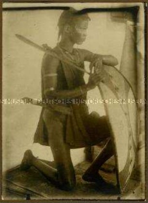 Seitenansicht eines hinter seinem Schild knienden Massai-Kriegers