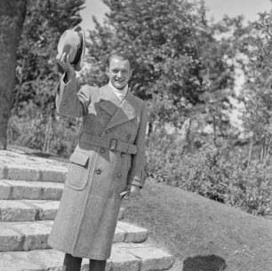Mann in Hut und Mantel im Park vor einem Denkmal