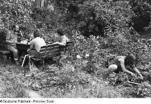 Drei Personen an einem Tisch und die Schriftstellerin Elke Erb bei der Gartenarbeit, aufgenommen in Hochkirch-Wuischke