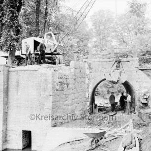 Brücke des Mühlenredder über dem Abfluss des Schlossgrabens: Renovierung: Seitenansicht von Süden: kein Durchfluss, Pumpe: Kran mit Greifarm, Arbeiter, Schubkarre, Baumaterial