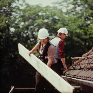 Zimmerer mit Holzbohle auf einem Gerüst
