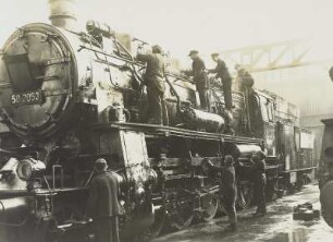 Güterzug-Lokomotive 58 2053 der Deutschen Reichsbahn. Auf und an der Lokomotive sieben Frauen und Männer beim Putzen, an der Stirnseite Emblem der FDJ : Dresden-Friedrichstadt. Reichsbahnausbesserungswerk. Güterzug-Lokomotive 58 2053 der Deutschen Reichsbahn. Auf und an der Lokomotive sieben Frauen und Männer beim Putzen, an der Stirnseite Emblem der FDJ