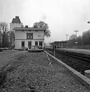 Bahnhofsgebäude, parkende Autos: rechts Bahnsteig, Gleise: im Hintergrund links Silo der Firma Ströh: im Vordergrund Freifläche mit Schotter, Absperrband