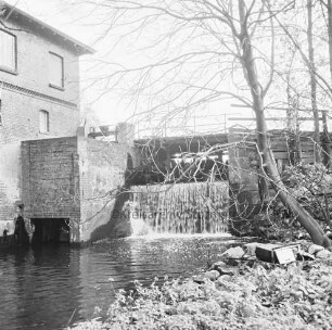 Mühlenwehr zwischen Mühlenteich und Glinder Au: darüber baufällige Brücke der Mühlenstraße: rechts Bäume: links Mühlengebäude