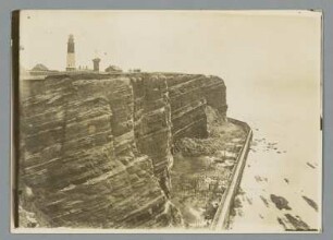 Die Westküste vor Helgoland : Blick auf die Klippen mit vorgelagerter Schutzmauer, im Hintergrund der Leuchtturm