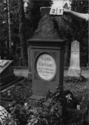 Grabstein 27 (Index: 99792859) Material: Sandstein und Marmor Zustand: Sockel und Giebel stark verwittert Maße HxBxT: 163x54x30 cm Beschreibung: Stele, Sockel profiliert, Giebel mit Akroter, Schriftfeld eingetieft, stehendes Oval, eingesetzte Textplatte Symbolik: Efeubätter: Grabstein 27