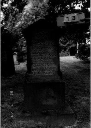 Grabstein 13 (Index: 100110215) Material: Sandstein Zustand: verwittert Maße HxBxT: 135x73x45 cm Beschreibung: Stele, getreppter Sockel, giebelartiger Abschluß mit Verdachung: Grabstein 13