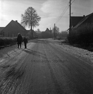 Tremsbüttel-Dorf: Hauptstraße: links Frau mit Kind: hinten Bauernhäuser und Wohnhäuser mit Vorgärten: rechts Strommasten: links Baum: Winter