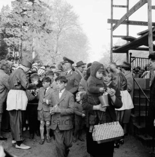 Schlosspark: Ostereiersuchen: als Osterhase verkleidetes Mädchen beim Verteilen von Süßigkeiten an die Kinder: Polizisten: rechts Gerüst von Schlossfassade: im Vordergrund Mutter mit Kleinkind auf Arm