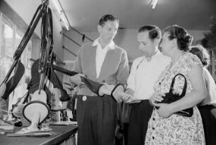 Drei Personen begutachten einen auf der Leipziger Herbstmesse 1955 ausgestellten Staubsauger