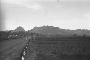 Permokarbon Hänge : Landschaft mit Hütten, einem Graben und Palmen. Im Hintergrund Berglandschaft