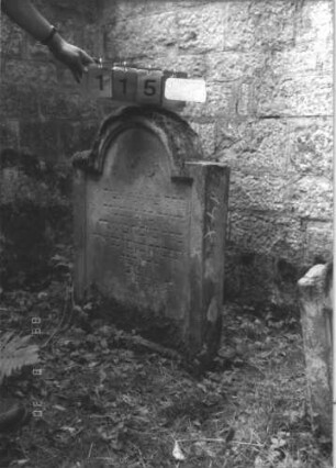 Grabstein 115 (Index: 99609751) Material: Sandstein Zustand: verwittert Maße HxBxT: 92x66x14 cm Beschreibung: Stele, eingezogener Rundbogenabschluß, Schriftfeld eingetieft Besonderheit: Kindergrab: Grabstein 115