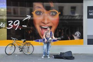 Lausanne - Straßenmusiker : Ein Straßenmusiker spielt vor einem überdimensionalen Werbeplakat in der City. Aufgenommen am 20. Mai 2010 in Lausanne