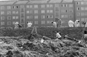 Baustelle vor einem bereits bewohnten Wohnblock. Maurer beim Hochziehen einer Ziegelwand