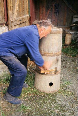 Kurt Franz demonstriert Festschlagen eines Reifens an einem Wasserfass; das Fass diente früher zum Waschwasserholen an einer Quelle am Mosbacher Weg