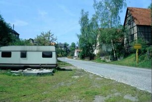 gepflasterte Straße mit Ortsschild, giebelständige Häuser