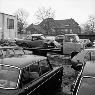 Hof des Abschleppdienstes am Waldemar-Bonsels-Weg: nach Verkehrsunfall: Wrack von Unfall-Pkw auf Plattform von Abschleppwagen: rundum abgestellte Pkws: hinten links: Werkstattgebäude, hinten Mitte: U-Bahnhof Ahrensburg West