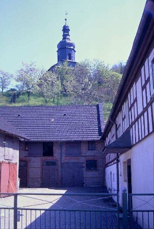 Blick in einen Hof, hinten Scheune, darüber Kirche auf dem Hang
