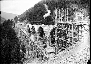 Alter Viadukt mit einem darauf befindlichen Eisenbahnzug, Fahrgerüst und im Bau befindliche Bögen