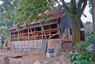 Dorfplatz (2): Fachwerkscheune: Sanierung: Traufseite, unten Gefache mit neuer Ausmauerung, oben Blechverkleidung abgenommen, Blick in Innenraum: Giebelseite, Gefache mit neuer Ausmauerung, Scheunentor, oben Blechverkleidung: davor Blechplatten, Backsteine, Arbeitsbühne, Leiter, Werkzeug: Baum, Mann: Juli 1994