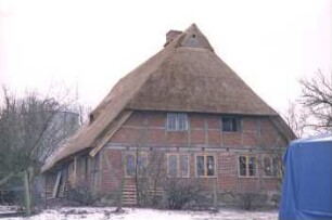 Eichede: Lindenallee 27: Fachwerkkate mit Feldsteinfundament, Reetdach: nach Neueindeckung: Giebelseite Wohntrakt, an Giebel Eulenloch: Traufseite mit Tür: vor Hauswand Holzpaletten: im Hintergrund Silo