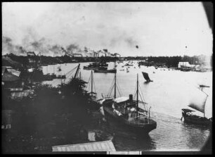 Boote auf dem Fluss : Thailand. Blick auf einen Fluss mit Schiffen und Booten sowie Industrieanlagen mit rauchenden Schloten am Ufer