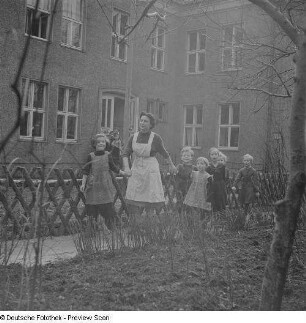 Kindergärtnerin mit Kindern vor dem Kindergartengebäude